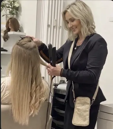 Friseurin glättet blondes Haar mit Glätteisen im Friseursalon.